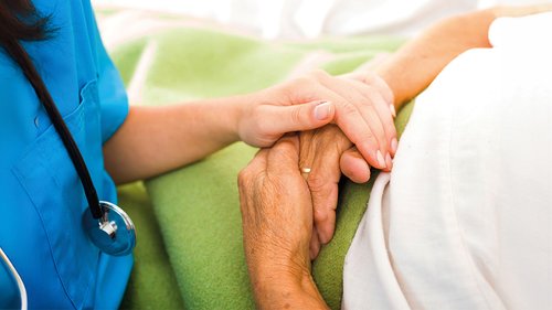 Pflegerin legt ihre Hand auf die einer alten Person 