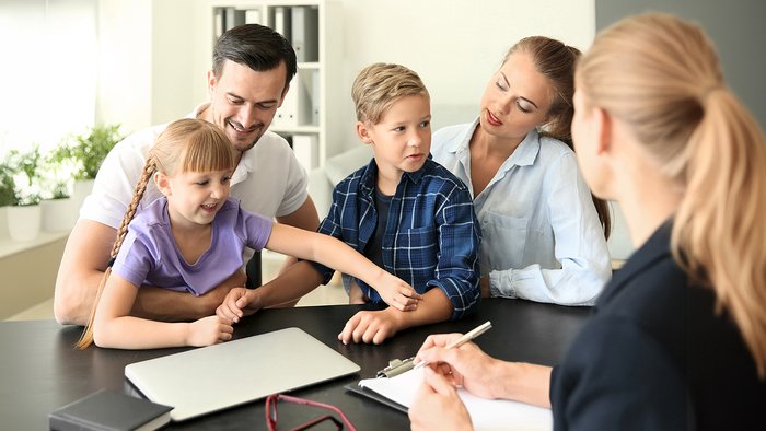 Familie sitzt einer Frau an einem Tisch gegenüber 
